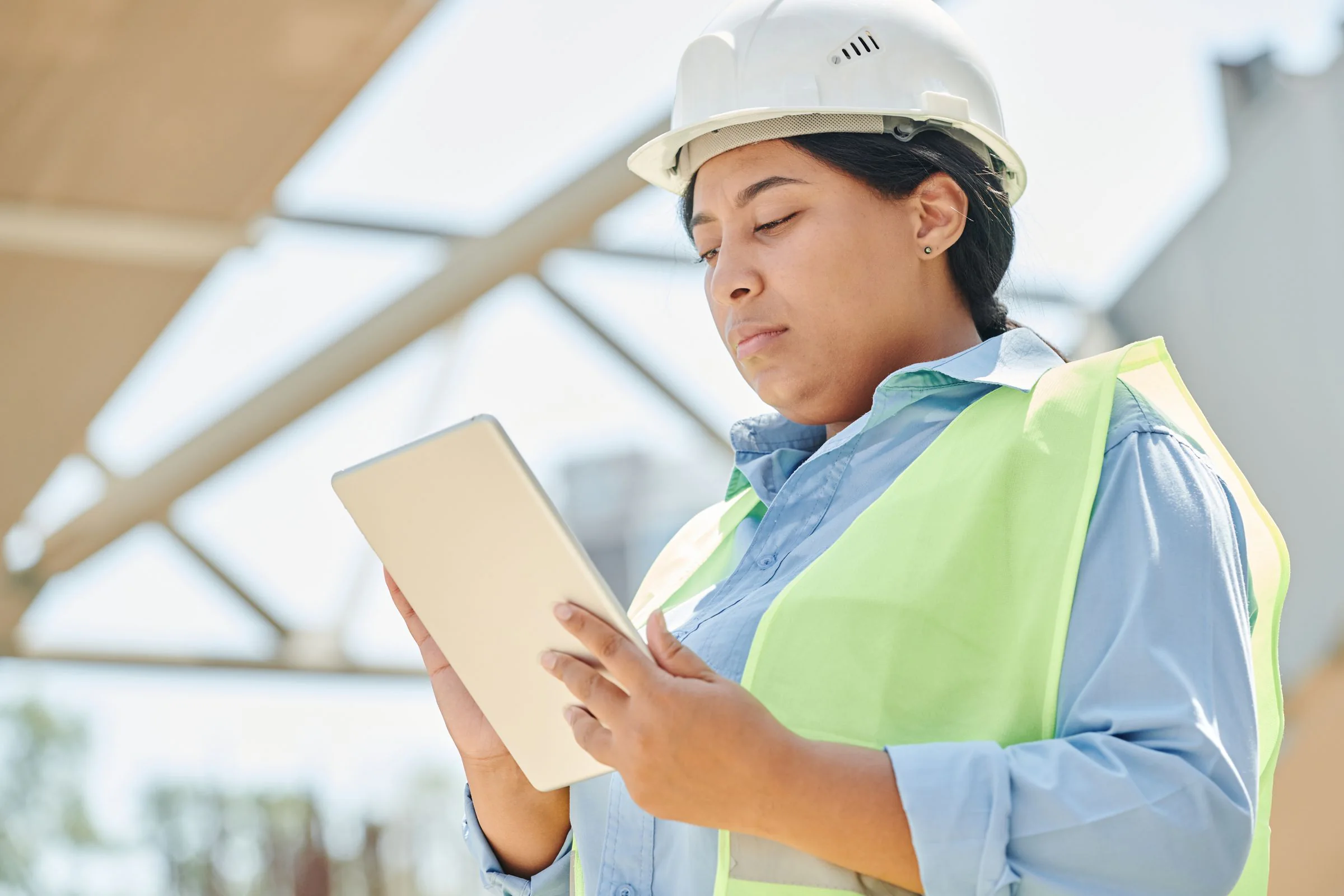 A safety professional in a hard hat and high-visibility vest reviewing site information on a tablet.