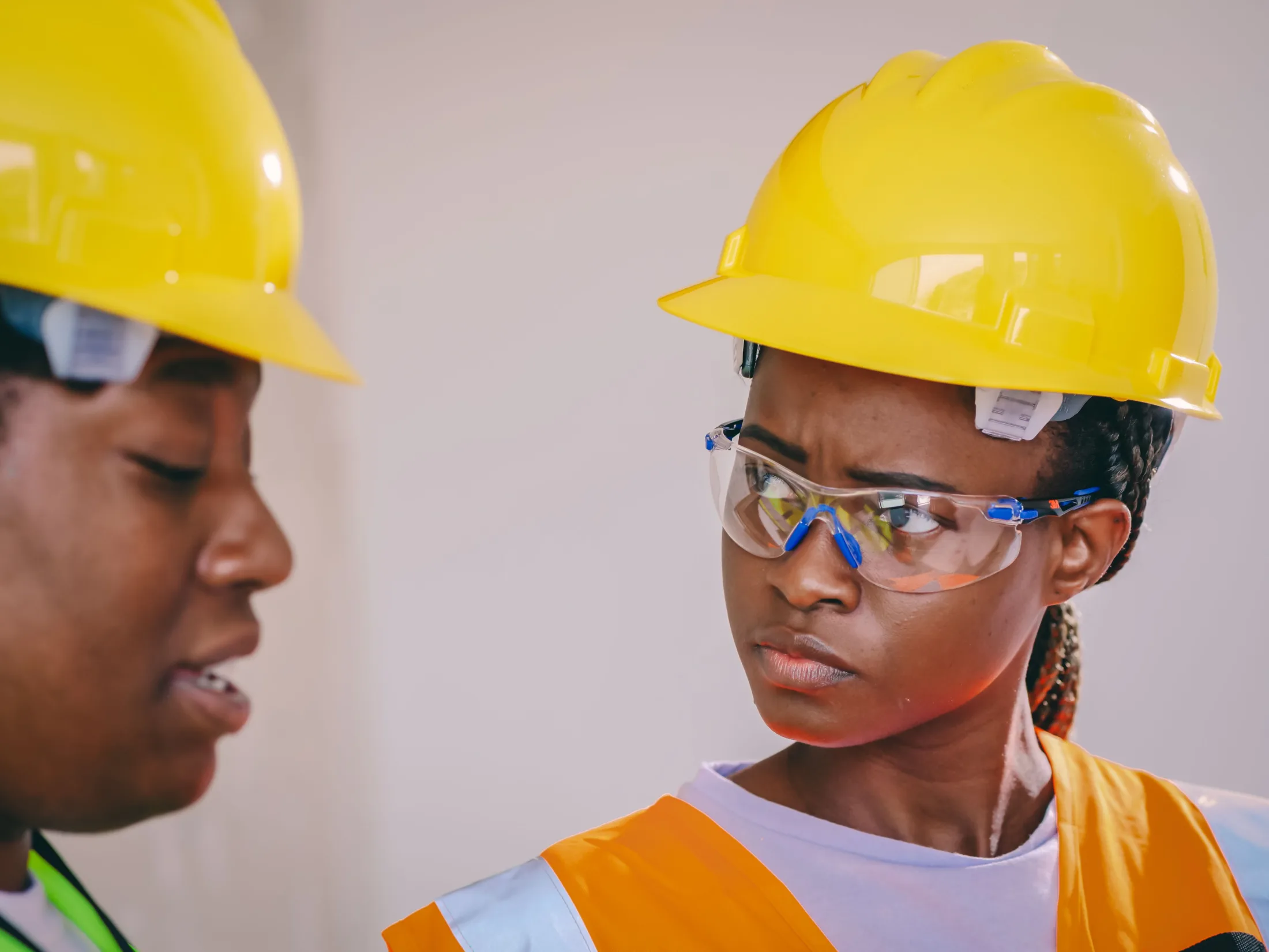 A worker wearing a hard hat and safety glasses listens during a workplace safety discussion.